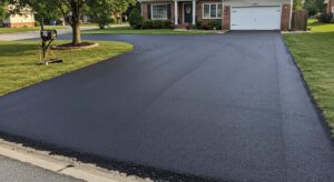 Workers resurfacing a residential asphalt driveway with paving equipment and fresh blacktop.