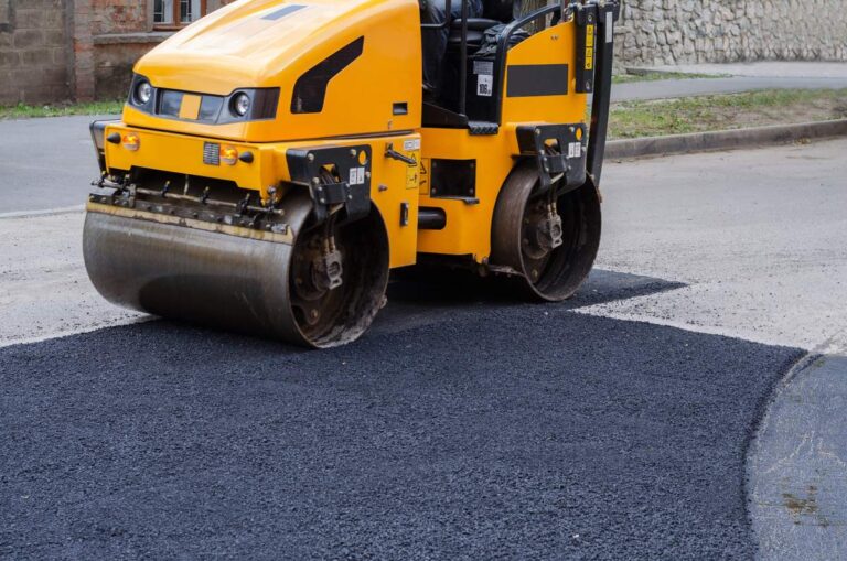 A homeowner clearing a driveway of debris and marking boundaries before asphalt paving work begins.
