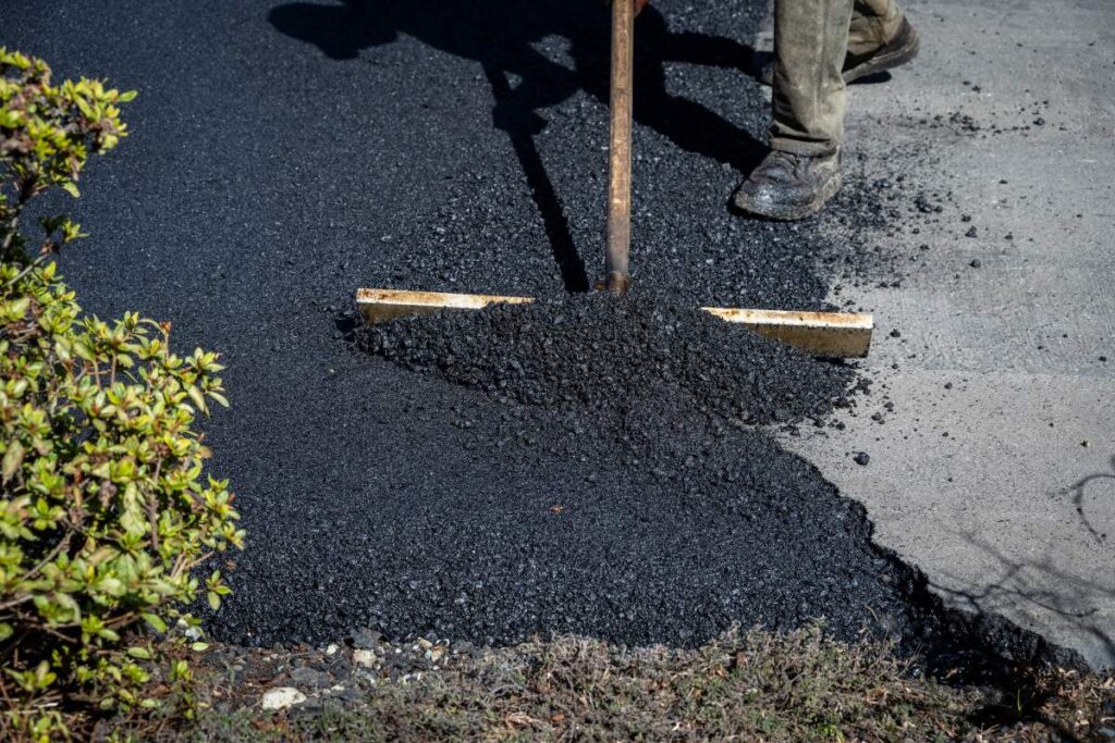 Residential asphalt driveway with recycled pavement texture, planted edges, and rainwater flowing toward a landscaped drainage area.