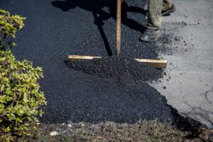 Residential asphalt driveway with recycled pavement texture, planted edges, and rainwater flowing toward a landscaped drainage area.
