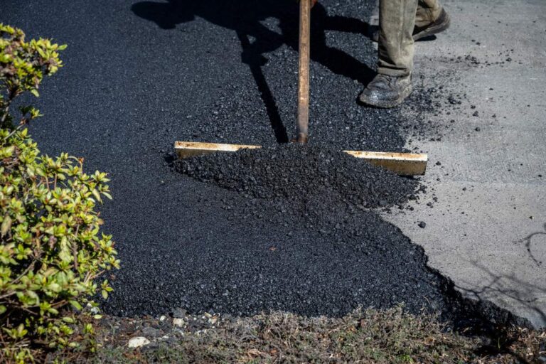 Residential asphalt driveway with recycled pavement texture, planted edges, and rainwater flowing toward a landscaped drainage area.